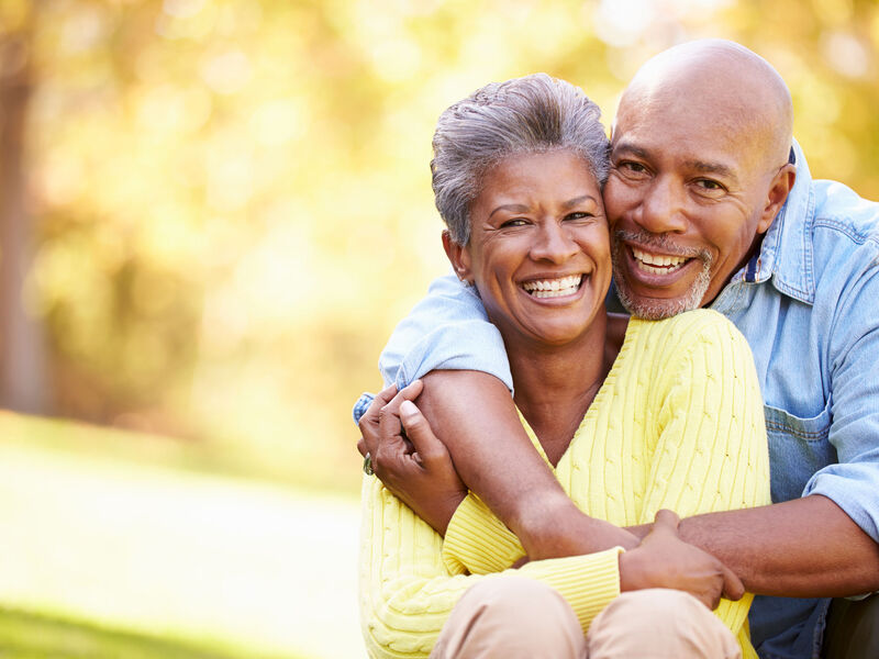 An image of a smiling couple sitting outside with their arms around each other