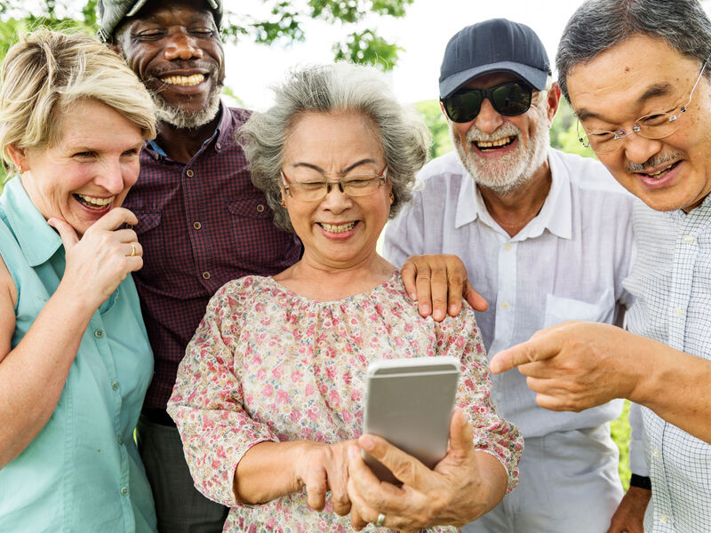 A group of laughing friends standing outside looking at the screen on one of their cell phones