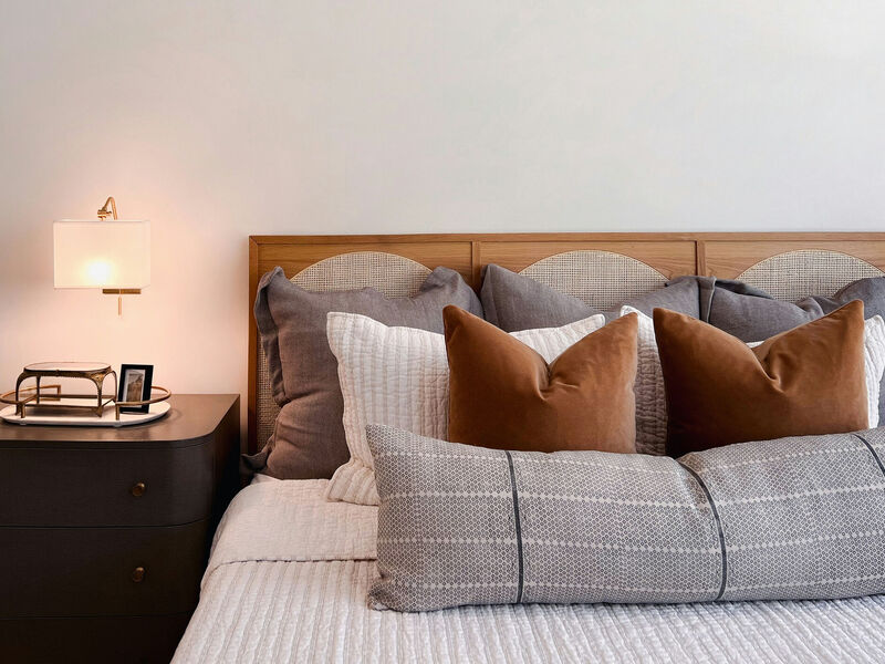 stock image of a bed with decorative pillows, next to a nightstand with lamp.