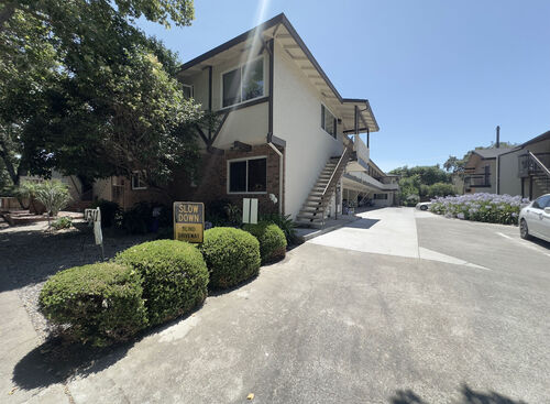 Apartment building with white walls brick accents and brown trim lined with green bushes