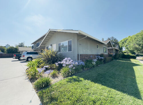 Green lawn surrounding a ranch style building with driveway on the left
