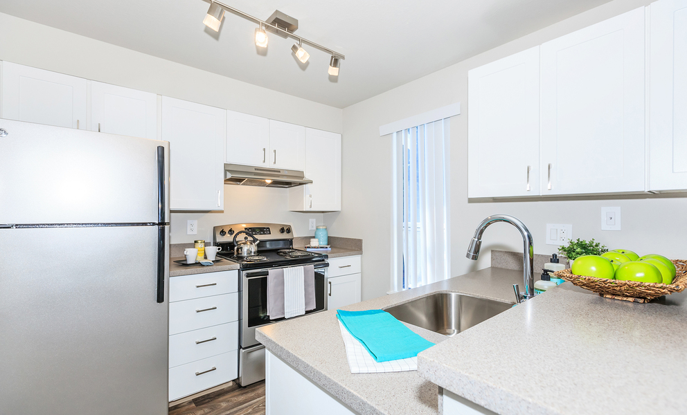 Image of kitchen featuring stainless steel refrigerator, stove and upgraded lighting with white cabinets.