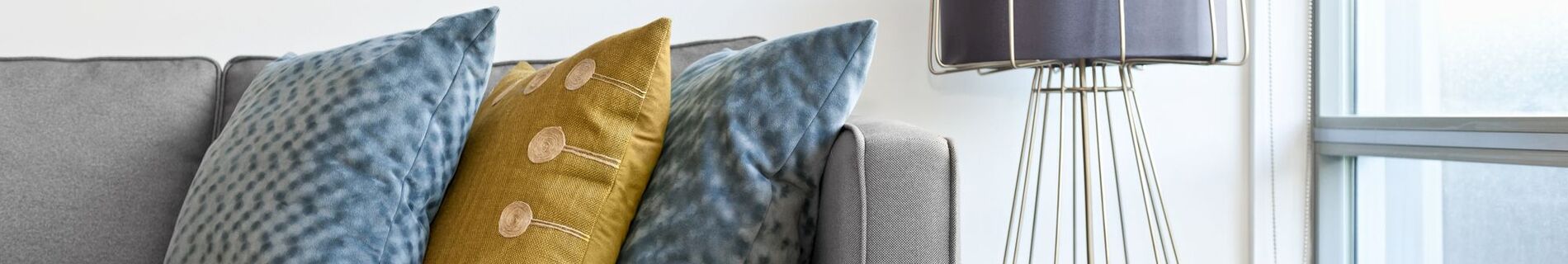 Grey couch and side table with colorful pillows by a window