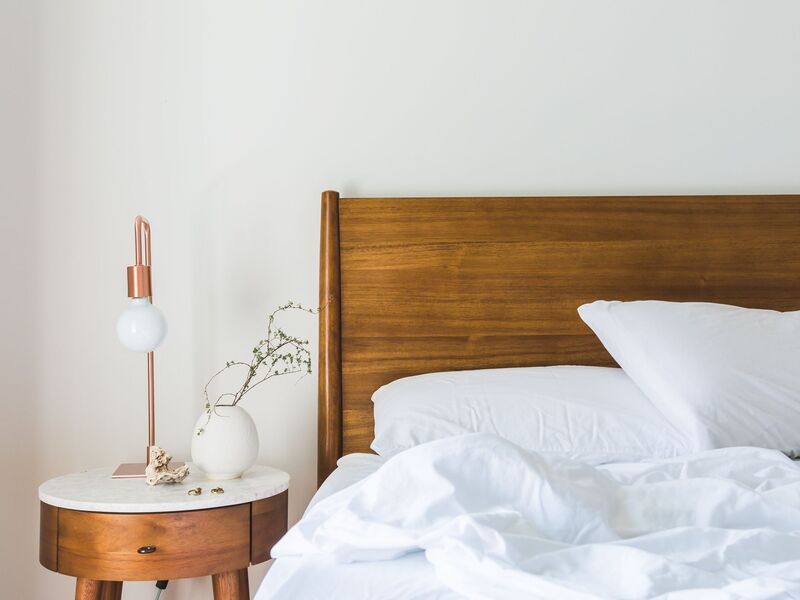 Wood headboard and bed with nightstand that has lamp and plant on top.