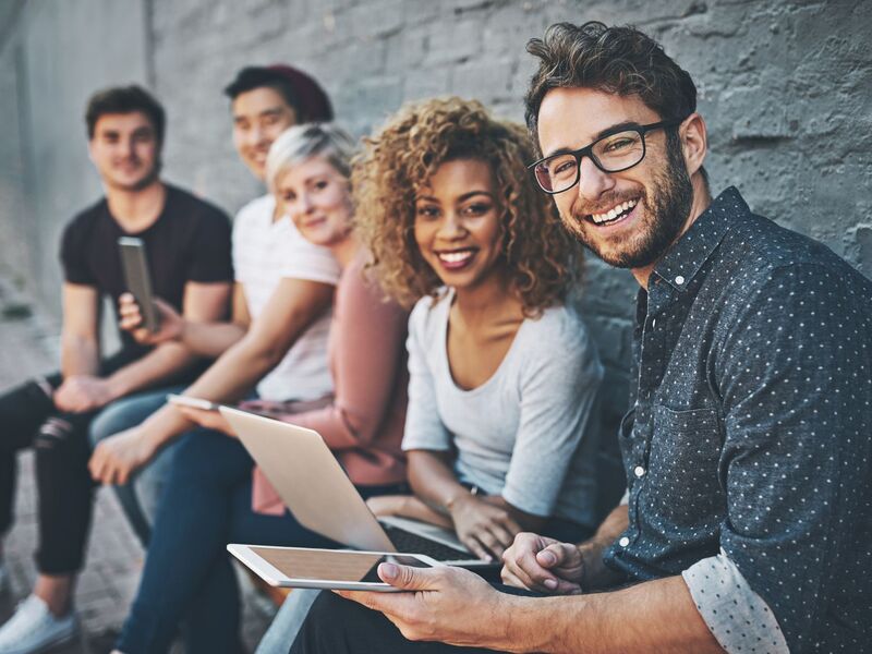 Diverse group on individuals using electronic devices and smiling at the camera