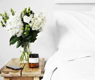 Stock image of a bed with flowers on a small table.