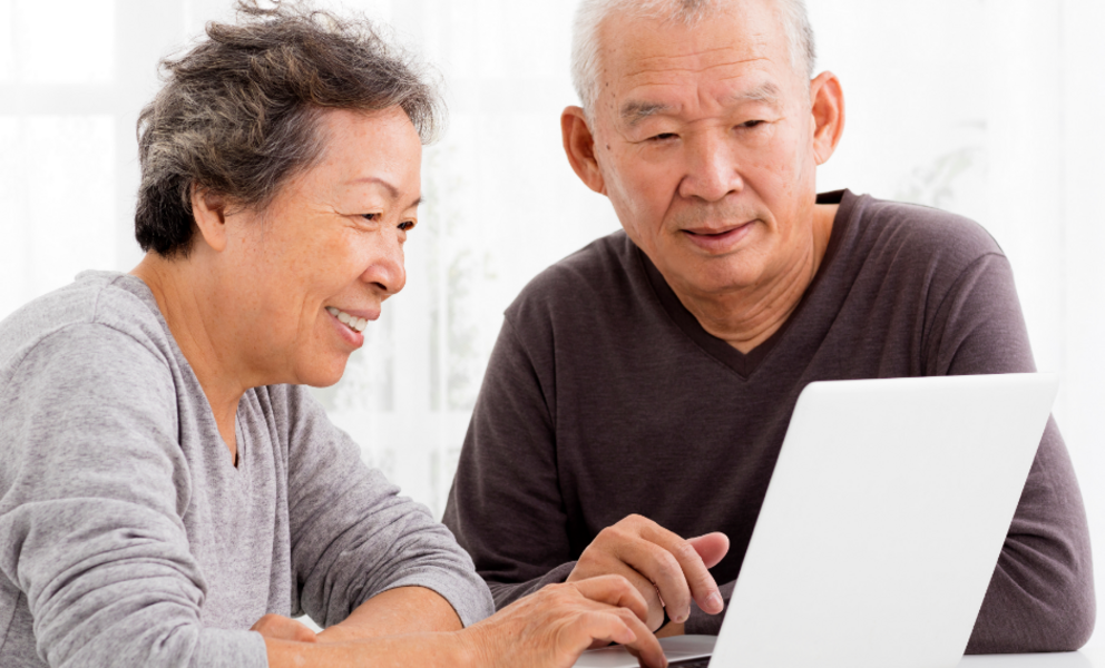 A couple sitting at a table together, looking at a laptop