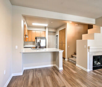 Interior image of model apartment living room facing fireplace, kitchen, and stairs