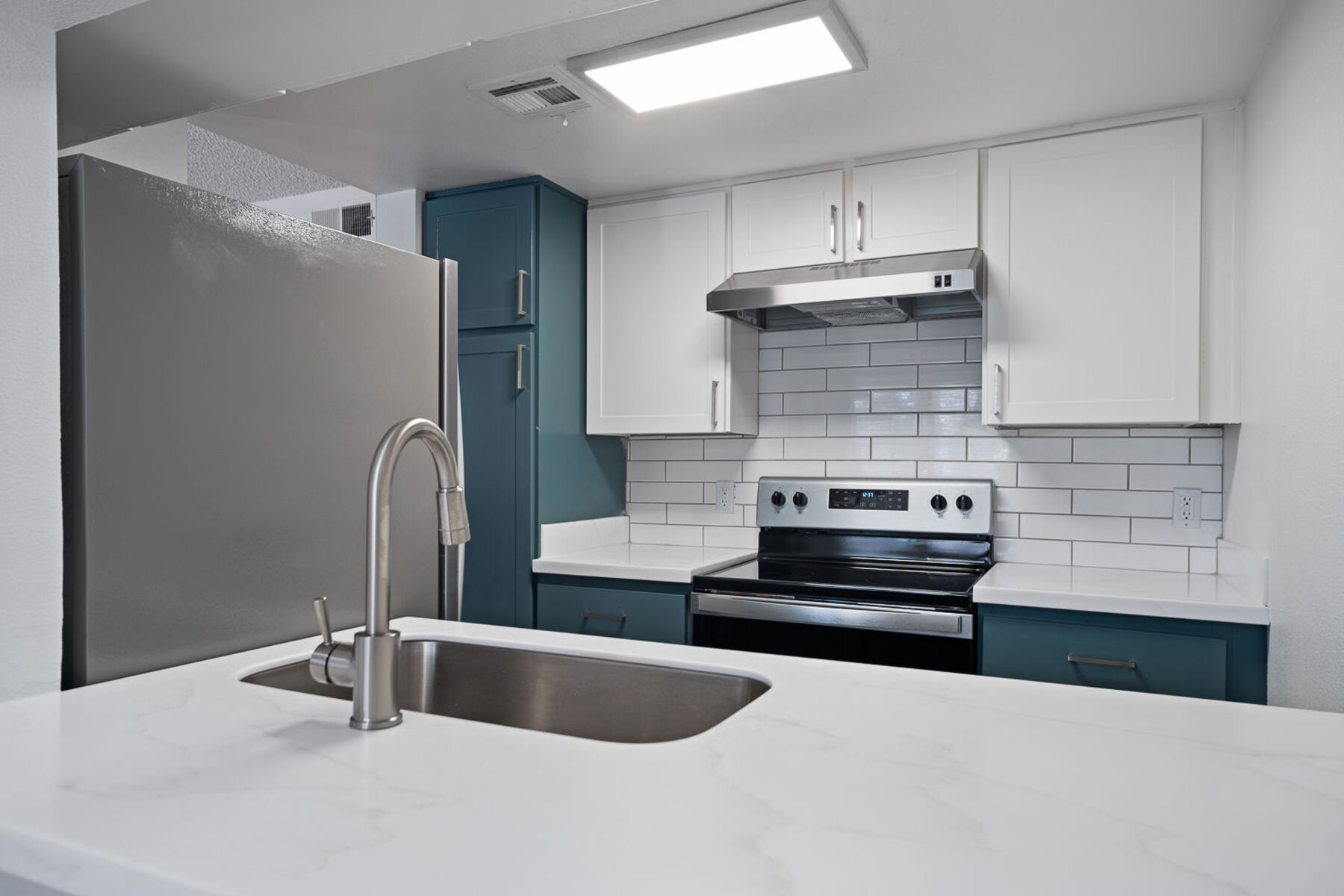 Kitchen with light countertops, a refrigerator and a stainless steel range.