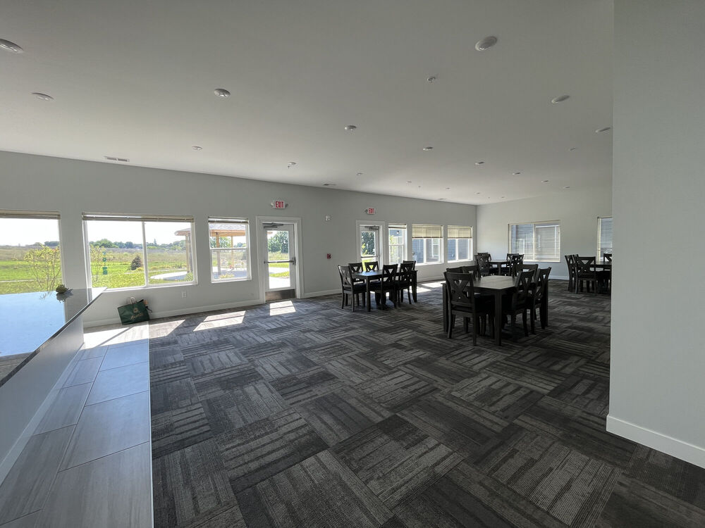 Picture of the community room with tables and ample natural light from windows in the Alice Place Senior Living Apartments in Monroe, WI.