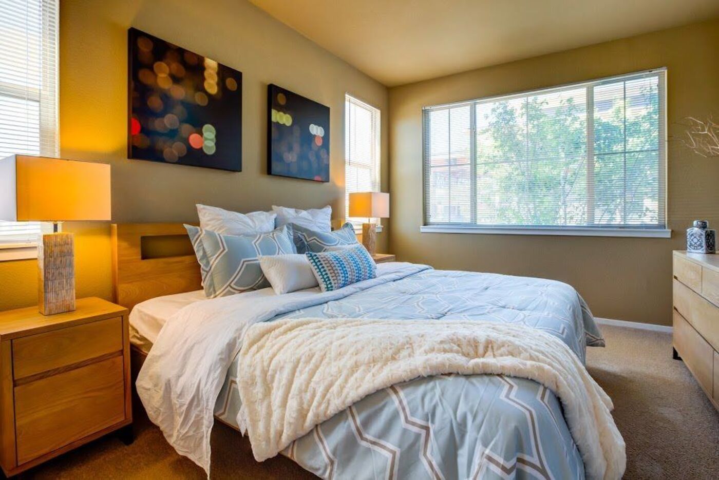 Prana Apartment Homes - Image of the model apartment bedroom with a bed, side table with a lamp, and plush carpeting.