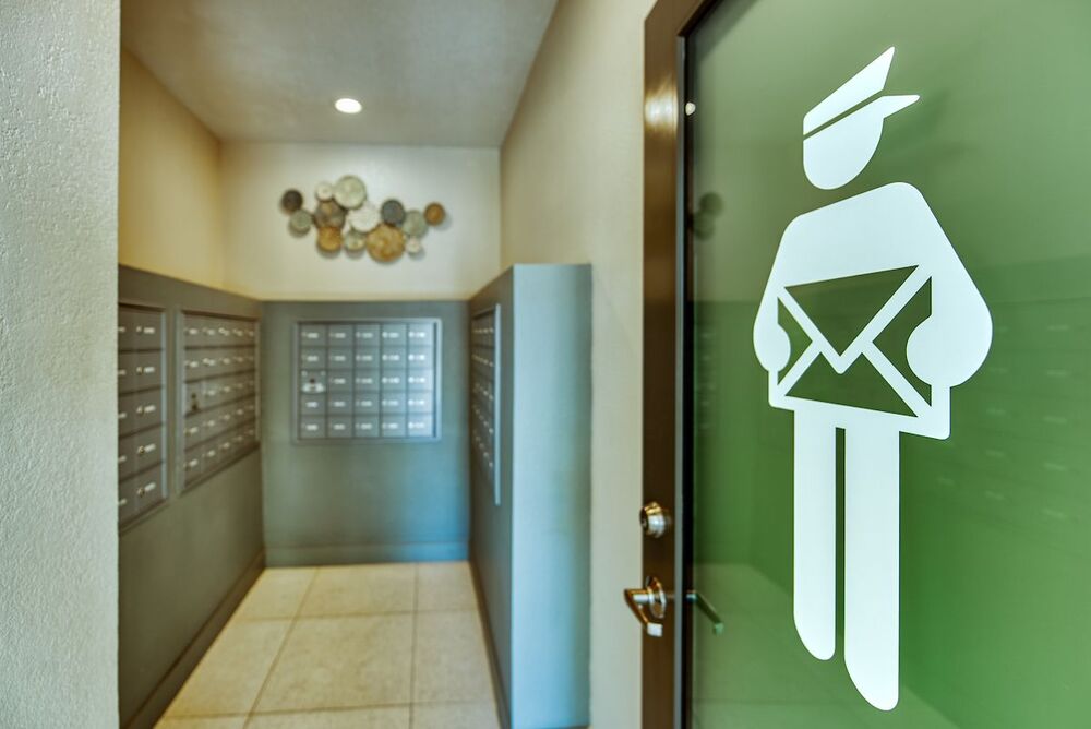 Community mail room with mail boxes, tile floor, and glass door with mail person icon.